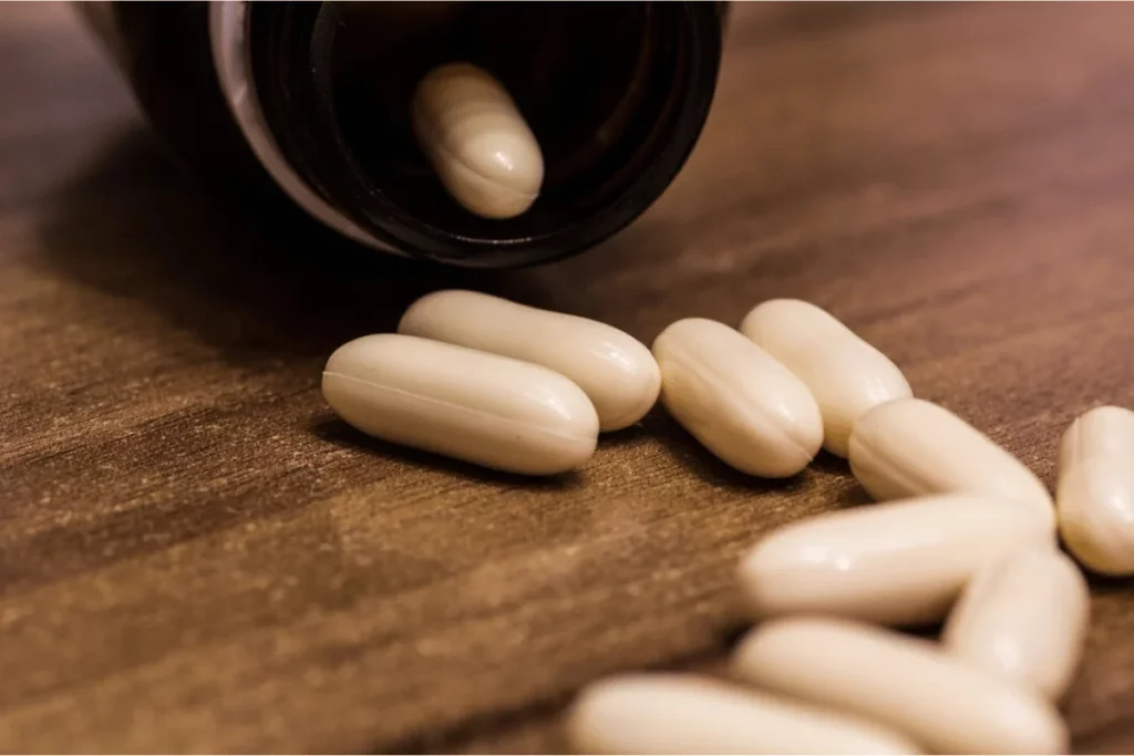 A bottle of white capsules tipped over on a wooden surface, with several capsules scattered nearby.