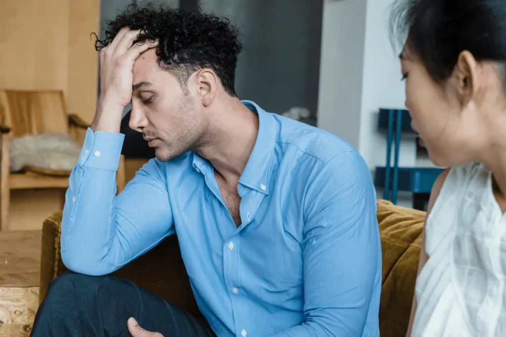 Stressed man in blue shirt holding his head during a serious conversation.