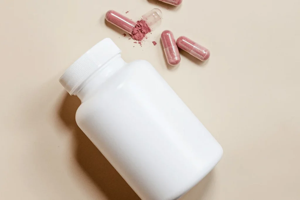 White supplement bottle with scattered pink capsules on a beige background.