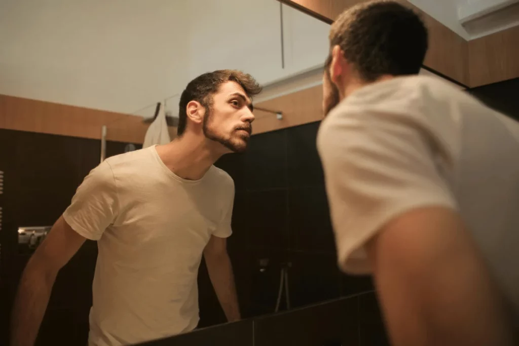 Young man examining his face in the bathroom mirror with a focused expression.