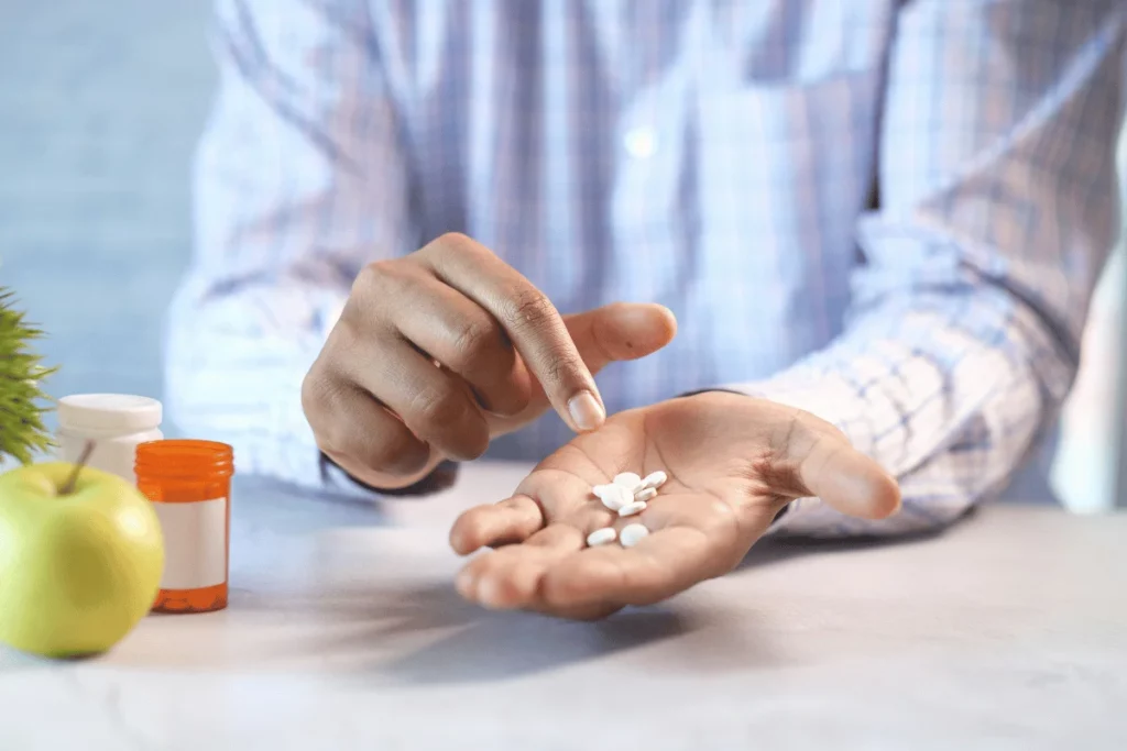 A person pointing at white pills in their open palm, with a focus on medication.