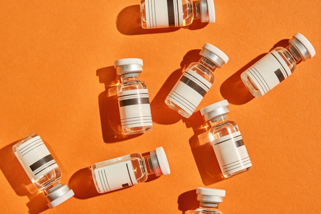 Multiple medical vials with white caps and labels are scattered across a bright orange surface.