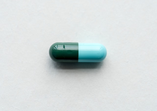 A single green and blue capsule pill sits alone on a plain white background.