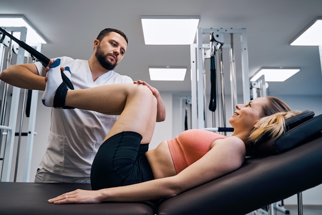 A male therapist performs leg stretching treatment on a female patient in a modern rehabilitation clinic.