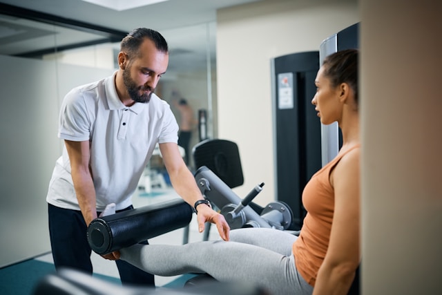 A physical therapist uses a percussion massage device on a woman's leg in a clinical setting.